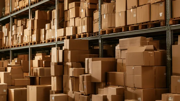 Warehouse aisle: an unstable pile of cardboard boxes stacked on the floor in front of shelved pallets